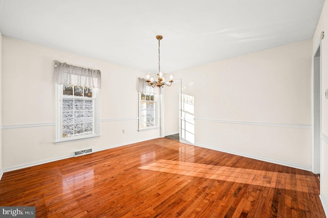 empty room with hardwood / wood-style flooring and an inviting chandelier