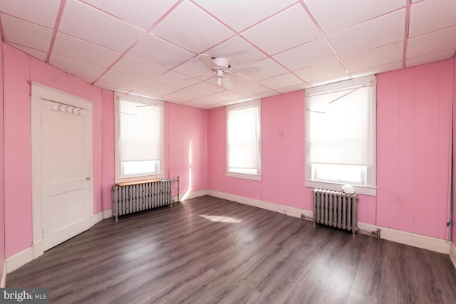 unfurnished room with a paneled ceiling, radiator, dark wood-type flooring, and ceiling fan