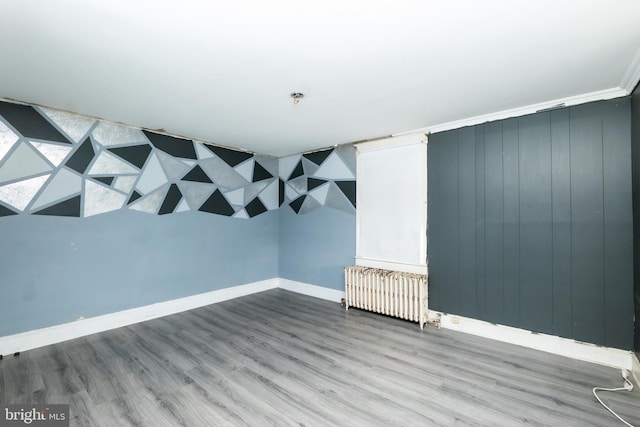 basement with wood-type flooring, radiator heating unit, and ornamental molding