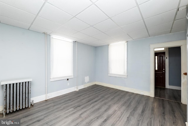 unfurnished room featuring a paneled ceiling, radiator heating unit, dark wood-type flooring, and a wealth of natural light