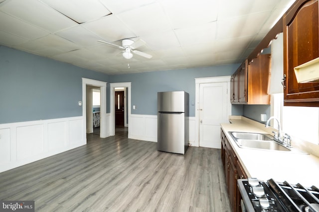 kitchen featuring stove, sink, ceiling fan, stainless steel fridge, and light wood-type flooring