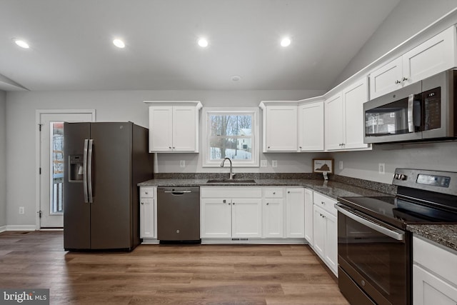 kitchen with appliances with stainless steel finishes, dark stone counters, sink, white cabinets, and light hardwood / wood-style floors