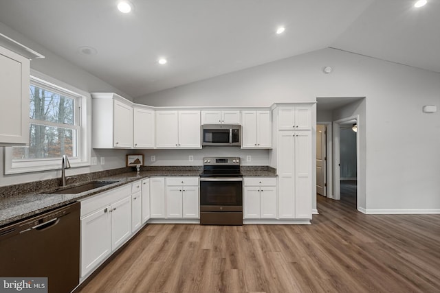 kitchen with white cabinetry, sink, stainless steel appliances, dark stone countertops, and light hardwood / wood-style floors