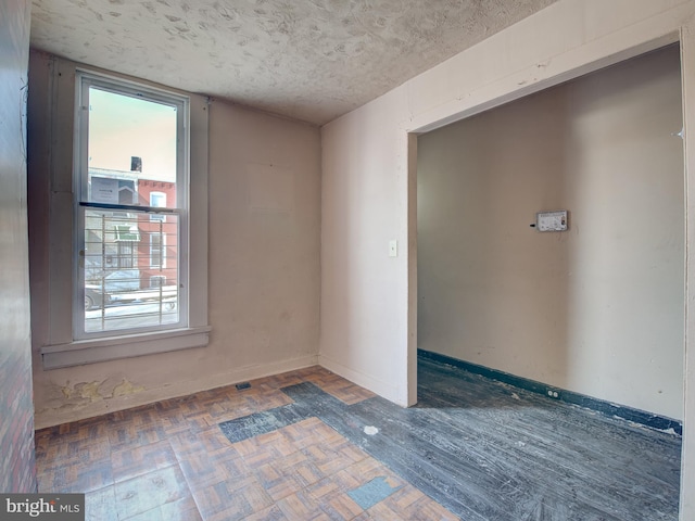 spare room featuring a textured ceiling and dark parquet floors