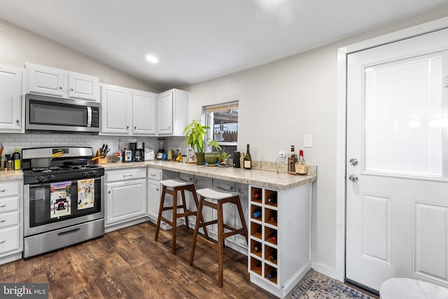 kitchen with stainless steel appliances, dark hardwood / wood-style flooring, lofted ceiling, white cabinets, and backsplash