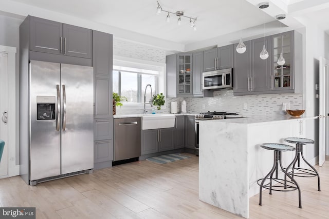 kitchen featuring kitchen peninsula, gray cabinetry, stainless steel appliances, sink, and decorative light fixtures