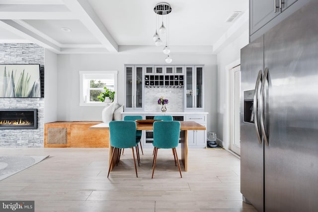 dining room with beamed ceiling, light wood-type flooring, a fireplace, and coffered ceiling