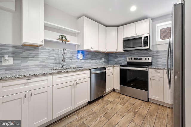 kitchen featuring sink, decorative backsplash, light stone counters, white cabinetry, and stainless steel appliances