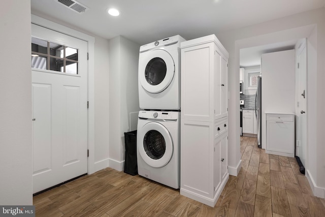 laundry room with stacked washer and dryer and light hardwood / wood-style flooring