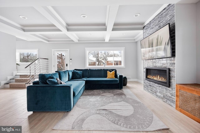 living room featuring coffered ceiling, a stone fireplace, light wood-type flooring, ornamental molding, and beamed ceiling