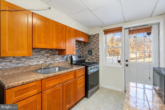 kitchen with a paneled ceiling, tasteful backsplash, gas stove, stone counters, and sink