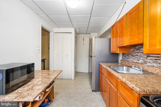 kitchen featuring stainless steel refrigerator, a paneled ceiling, sink, stove, and backsplash