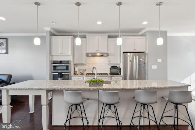 kitchen with white cabinets, stainless steel appliances, hanging light fixtures, and an island with sink