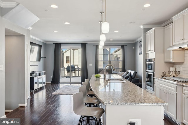 kitchen with a center island with sink, light stone countertops, white cabinetry, and sink