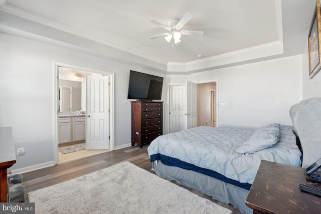 bedroom with ceiling fan, ensuite bathroom, light wood-type flooring, a tray ceiling, and ornamental molding