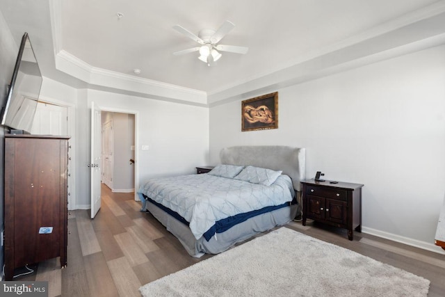 bedroom with hardwood / wood-style floors, a tray ceiling, ceiling fan, and ornamental molding