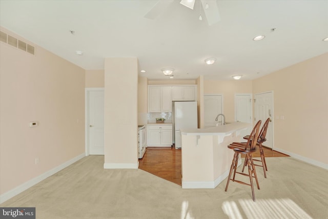 kitchen featuring white cabinetry, white appliances, a kitchen bar, a kitchen island with sink, and light colored carpet