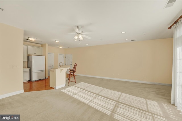 unfurnished living room with light colored carpet and ceiling fan