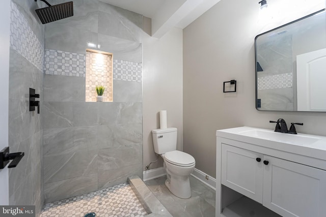 bathroom featuring a tile shower, vanity, and toilet