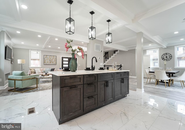 kitchen featuring dark brown cabinetry, a kitchen island with sink, beamed ceiling, and decorative light fixtures