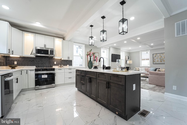 kitchen with beamed ceiling, an island with sink, pendant lighting, white cabinets, and appliances with stainless steel finishes