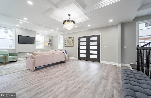 living room featuring a notable chandelier, light hardwood / wood-style floors, crown molding, and french doors