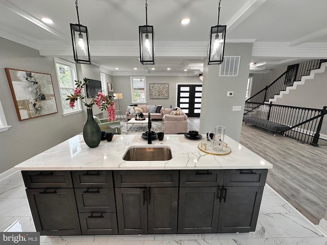 kitchen featuring a large island with sink, light stone counters, hanging light fixtures, and crown molding