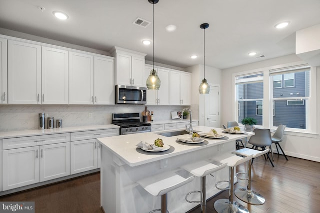 kitchen featuring pendant lighting, sink, appliances with stainless steel finishes, a kitchen island with sink, and white cabinets