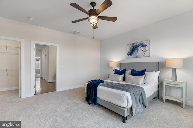 bedroom with a walk in closet, light colored carpet, ceiling fan, and a closet