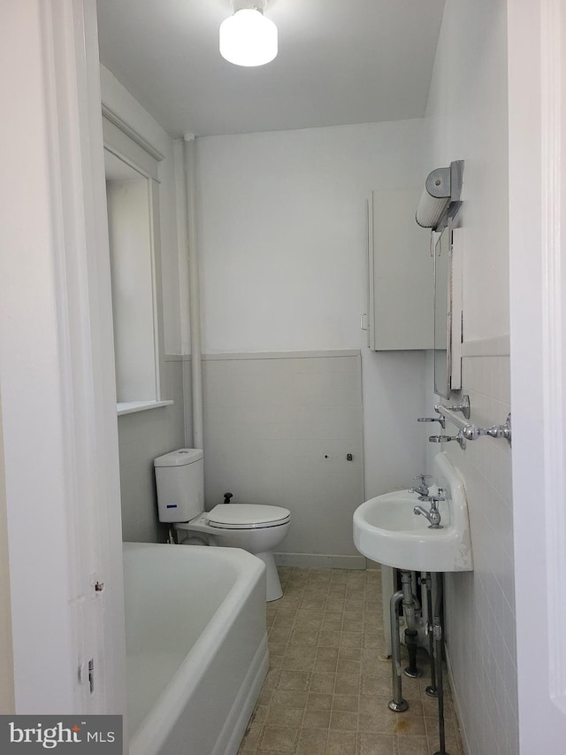 bathroom featuring a tub, tile walls, and toilet