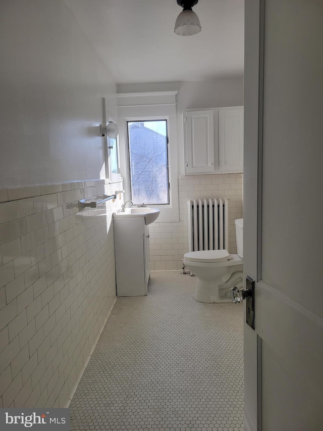 bathroom with radiator heating unit, tile patterned floors, toilet, vanity, and tile walls