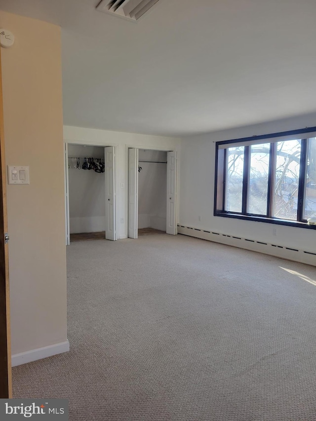 unfurnished bedroom featuring a baseboard radiator, multiple closets, and light colored carpet