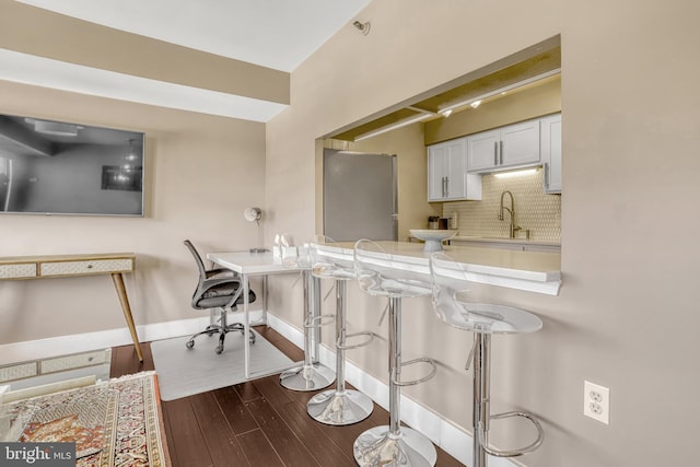 kitchen featuring a breakfast bar area, backsplash, white cabinets, dark hardwood / wood-style flooring, and kitchen peninsula