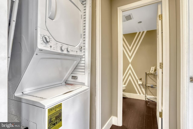 clothes washing area with stacked washer and dryer and dark wood-type flooring