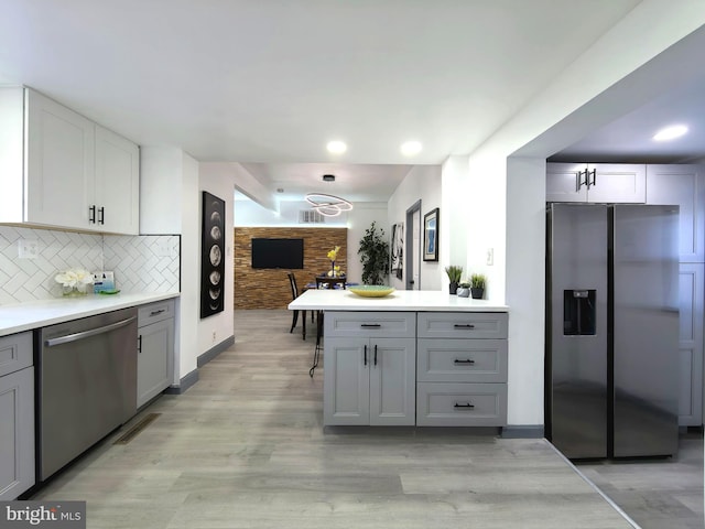 kitchen with backsplash, gray cabinetry, light hardwood / wood-style flooring, and appliances with stainless steel finishes