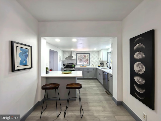 kitchen featuring wall chimney range hood, tasteful backsplash, a breakfast bar area, gray cabinets, and appliances with stainless steel finishes