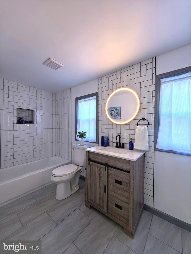 full bathroom with tiled shower / bath, vanity, a healthy amount of sunlight, and toilet