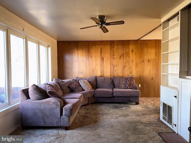 carpeted living room featuring ceiling fan and wooden walls