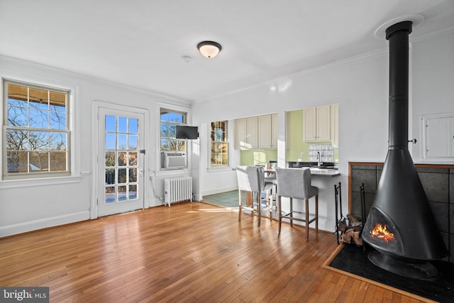 kitchen featuring a kitchen breakfast bar, ornamental molding, light hardwood / wood-style flooring, radiator heating unit, and a wood stove