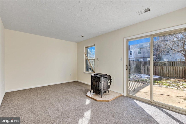 unfurnished living room featuring a textured ceiling, carpet, and a wood stove