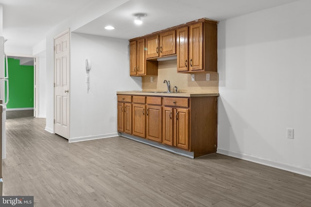 kitchen featuring light wood-type flooring, decorative backsplash, and sink