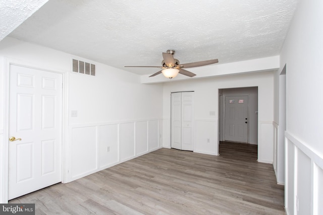 unfurnished bedroom featuring light wood-type flooring, a textured ceiling, ceiling fan, and multiple closets