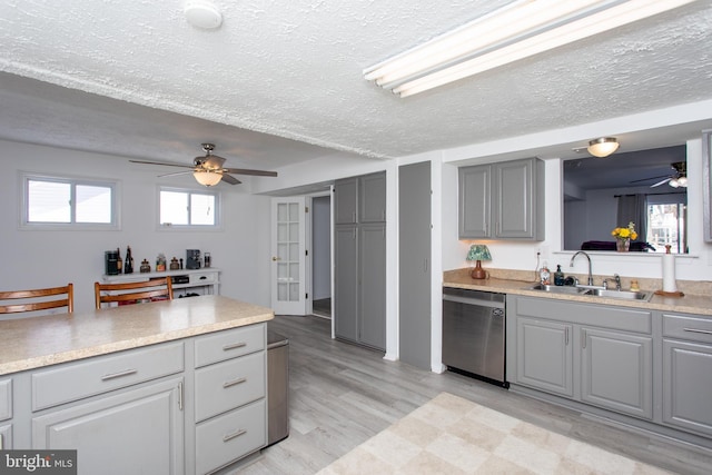 kitchen featuring gray cabinetry, dishwasher, sink, light hardwood / wood-style flooring, and a textured ceiling