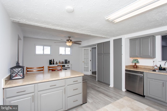 kitchen featuring gray cabinetry, ceiling fan, sink, stainless steel dishwasher, and a textured ceiling