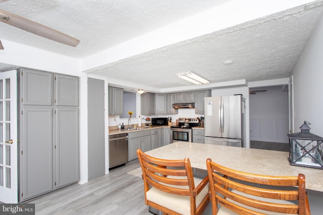 kitchen with sink, stainless steel appliances, light hardwood / wood-style flooring, a textured ceiling, and gray cabinets