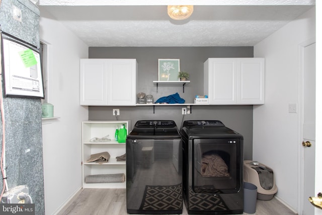 laundry room featuring cabinets, a textured ceiling, light hardwood / wood-style floors, and washer and clothes dryer