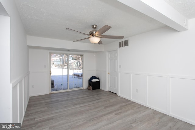 empty room featuring a textured ceiling, light wood-type flooring, ceiling fan, and beam ceiling