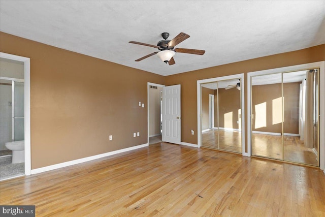 unfurnished bedroom featuring ensuite bathroom, light hardwood / wood-style flooring, ceiling fan, and multiple closets