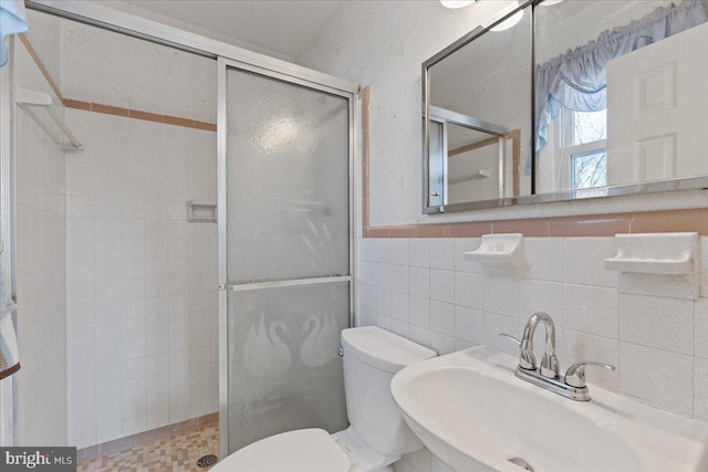 bathroom with sink, a shower with door, tile walls, and toilet