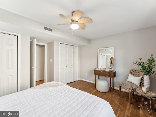 bedroom with dark wood-type flooring, ceiling fan, and multiple closets